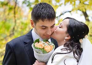 A couple shares a kiss while holding a bouquet of flowers, surrounded by autumn foliage. A couple shares a kiss while holding a bouquet of flowers, surrounded by autumn foliage.